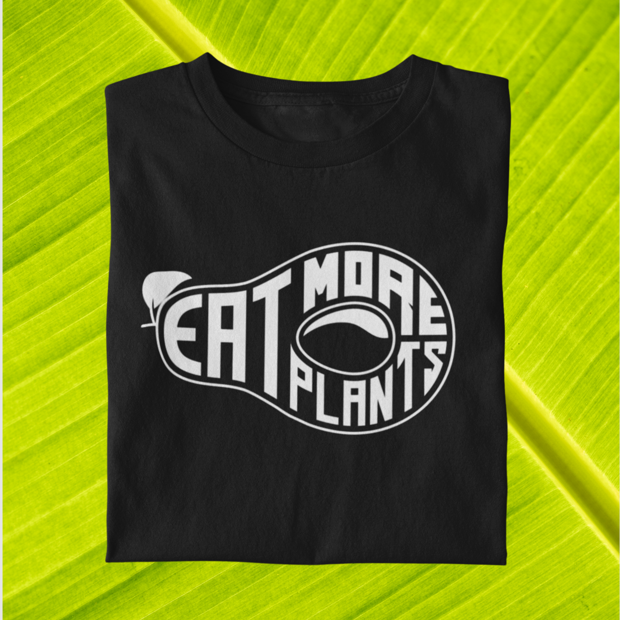 organic vegan t-shirts in black saying eat more plants, folded on leaf background