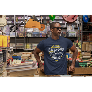 artistic young black man with sunglasses standing in book store with hanging musical instruments wearing bee vegan it's pretty sweet neon sign graphic design on navy colored vegan t shirt from vegan shirts from ethical clothing brands