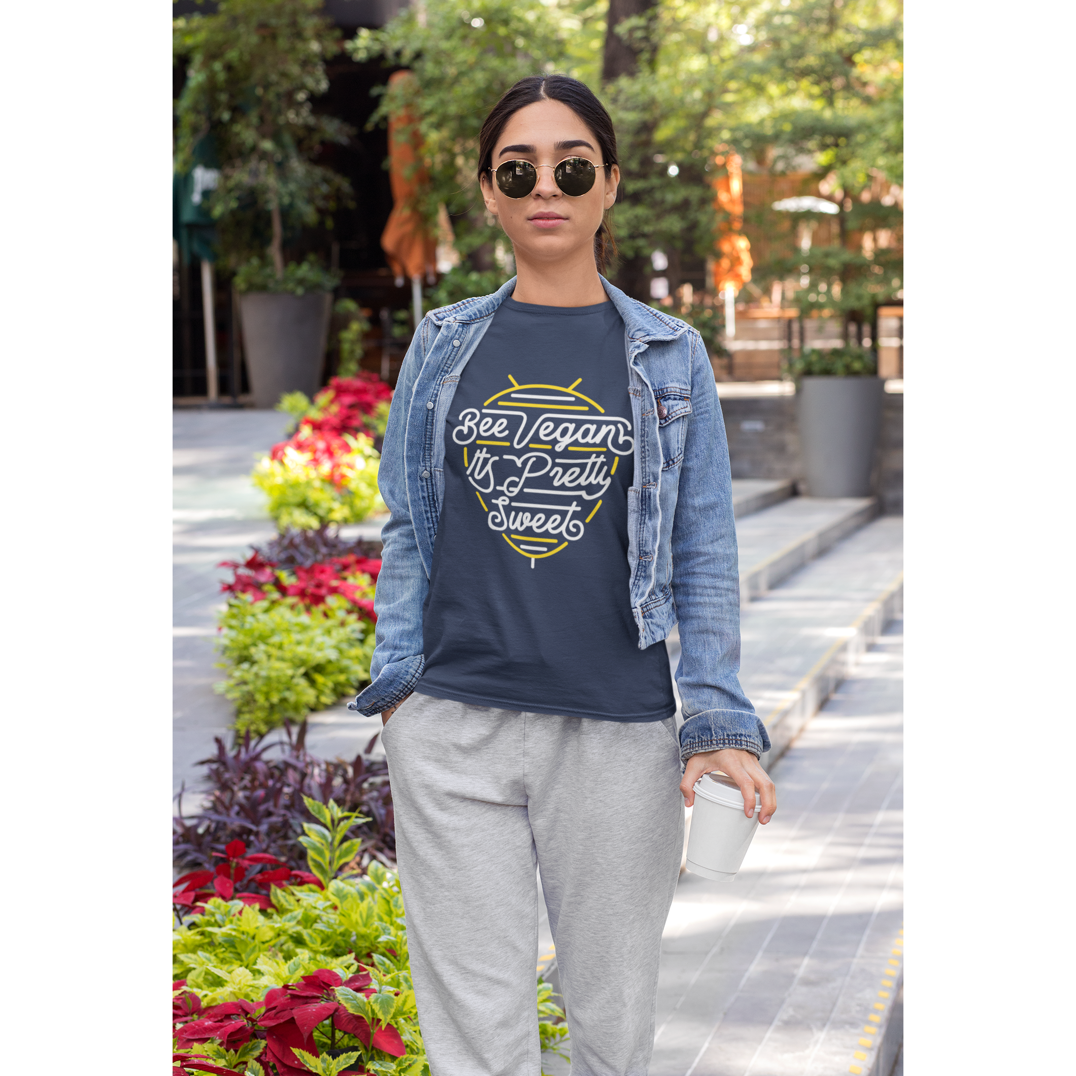 cool young Asian woman with sunglasses standing in front of plaza with flowers wearing bee vegan it's pretty sweet neon sign graphic design on navy colored vegan t shirt from vegan shirts from ethical clothing brands