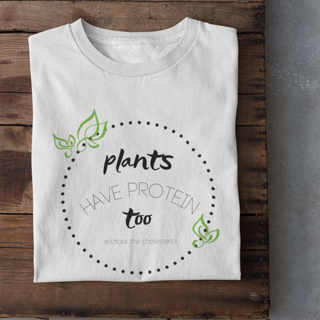 Plants have protein too ...without the cholesterol words in black with a black polka dot circle and green abstract leaves, design on a white premium tee folded on a wood table