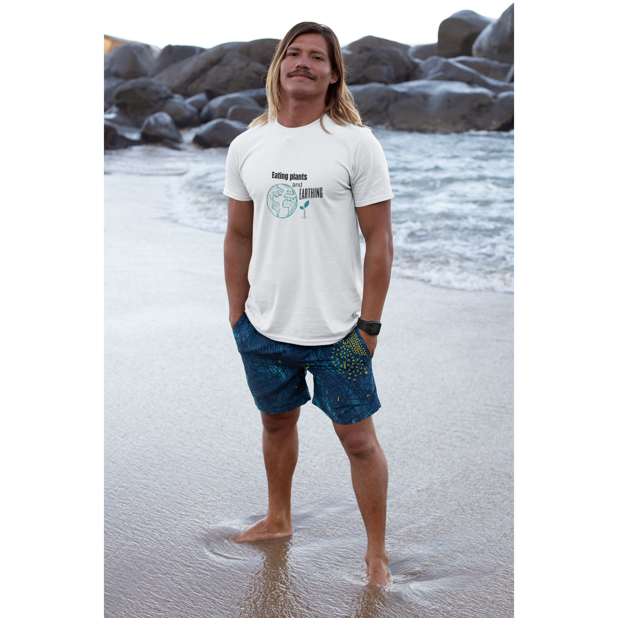 long haired man on beach wearing an eating plants and earthing vegan shirts design on a white color premium cotton t shirt for those who eat plants and enjoy their earthing mat