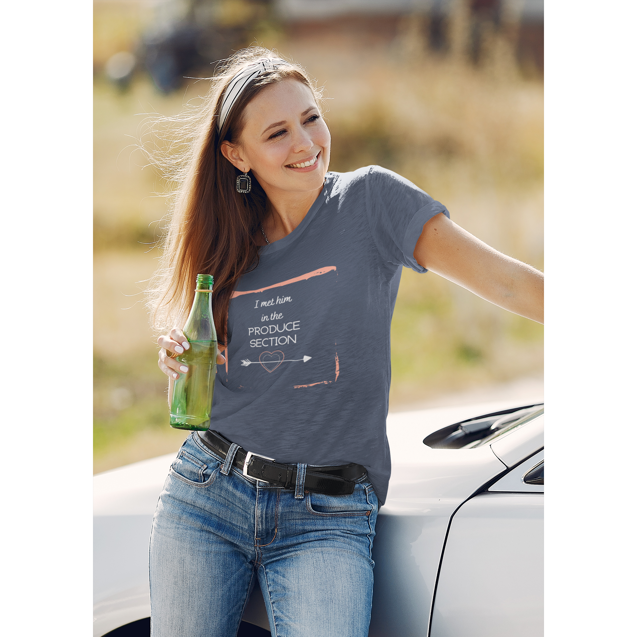 woman leaning on car wearing I met him in the produce section design with white words, arrow through a heart, and a pink frame, on a heather navy colored premium tee