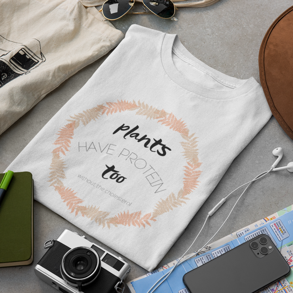vegan shirt design with black lettering and a circle made of tan and peach fern leaves, saying "plants have protein too without the cholesterol" on a white premium tee, folded flat with travel accessories