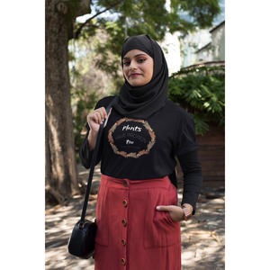 woman wearing hijab in a park, wearing a black colored vegan t shirt with white lettering and tan and peach fern circle, saying plants have protein too without the cholesterol