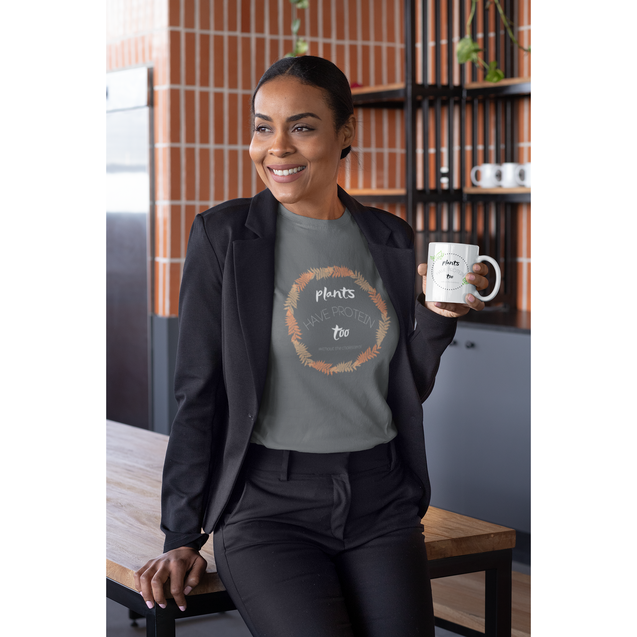 woman in professional black suit with a coffee mug, wearing an asphalt grey colored vegan t shirt with white lettering and tan and peach fern circle, saying plants have protein too without the cholesterol