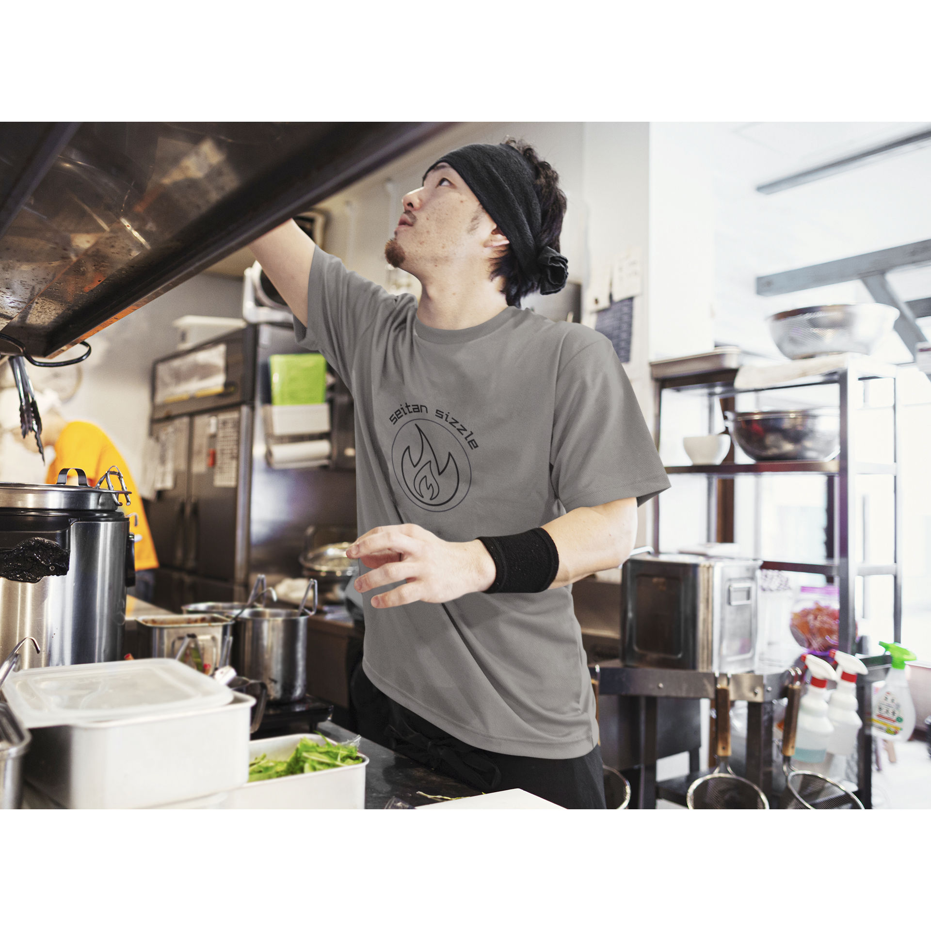 man cooking seitan recipes wearing asphalt vegan t shirt with black graphic saying seitan sizzle over a circle with a flame design, from vegan clothing brands