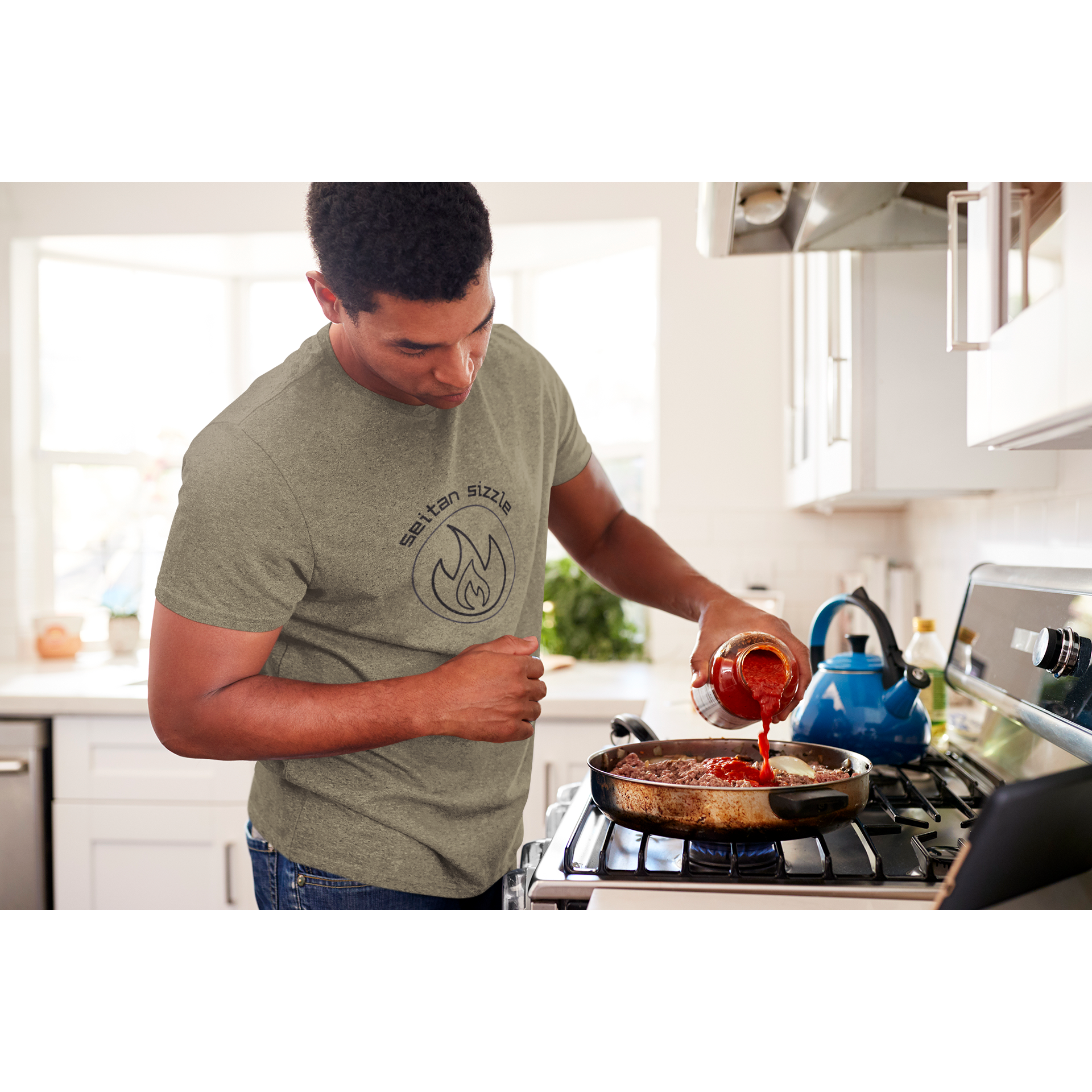 man cooking seitan recipes wearing heather olive colored vegan shirt with black graphic saying seitan sizzle over a circle with a flame design, from ethical clothing brands