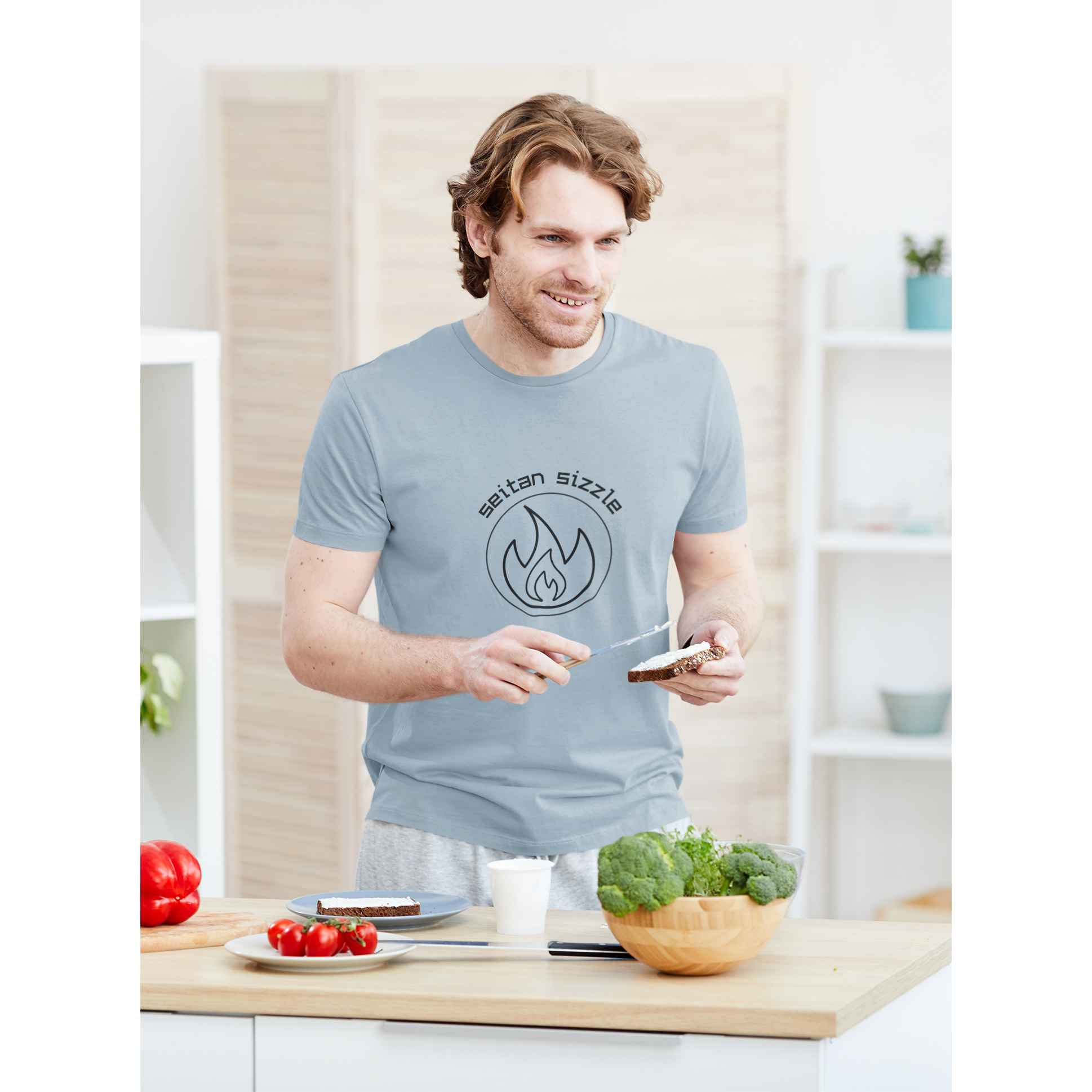 man cooking seitan recipes wearing light blue colored vegan shirt with black graphic saying seitan sizzle over a circle with a flame design, from ethical clothing brands and companies that donate to nonprofits