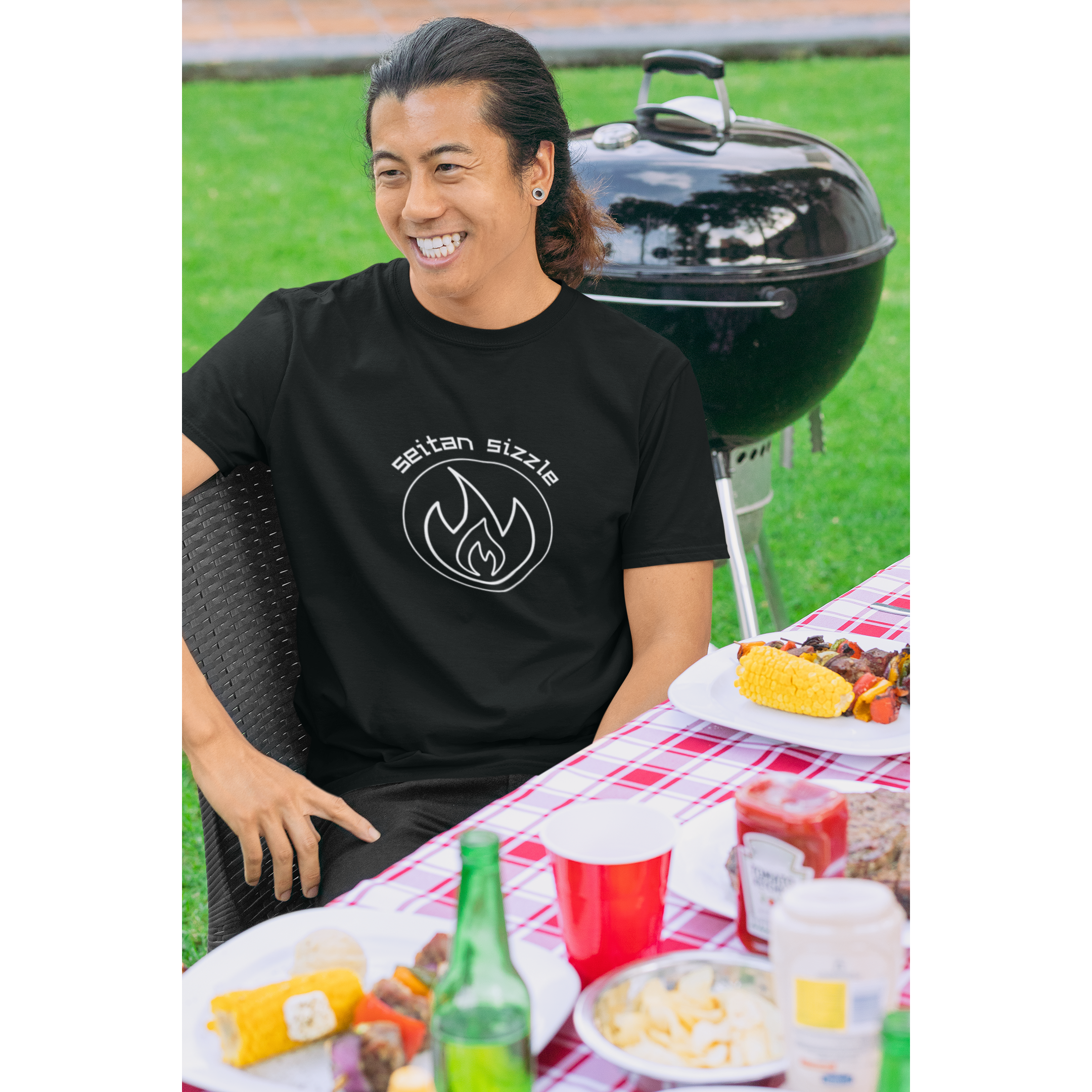 man grilling seitan recipes at a picnic wearing black colored vegan shirt with white graphic saying seitan sizzle over a circle with a flame design, from ethical clothing brands and companies that donate to nonprofits