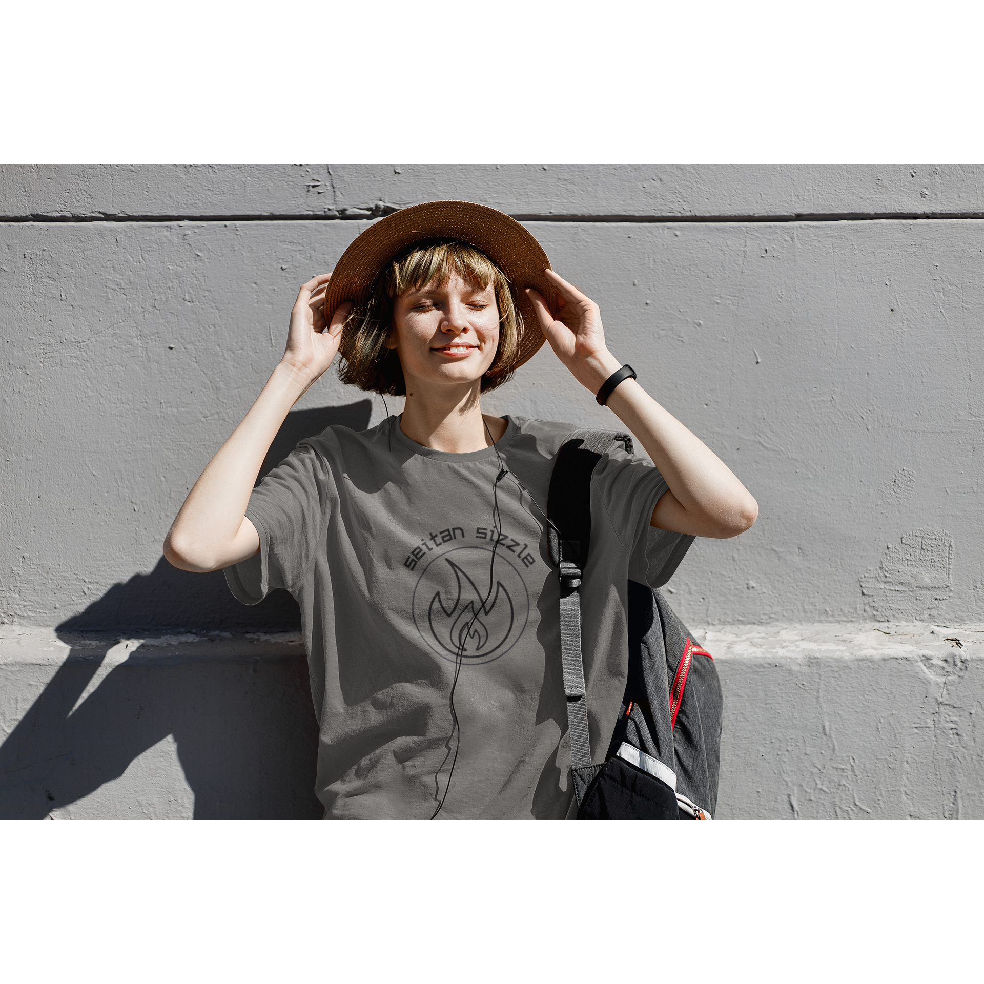 woman listening to music in the sunlight wearing asphalt colored vegan shirt with black graphic saying seitan sizzle over a circle with a flame design, from ethical clothing brands and companies that donate to nonprofits