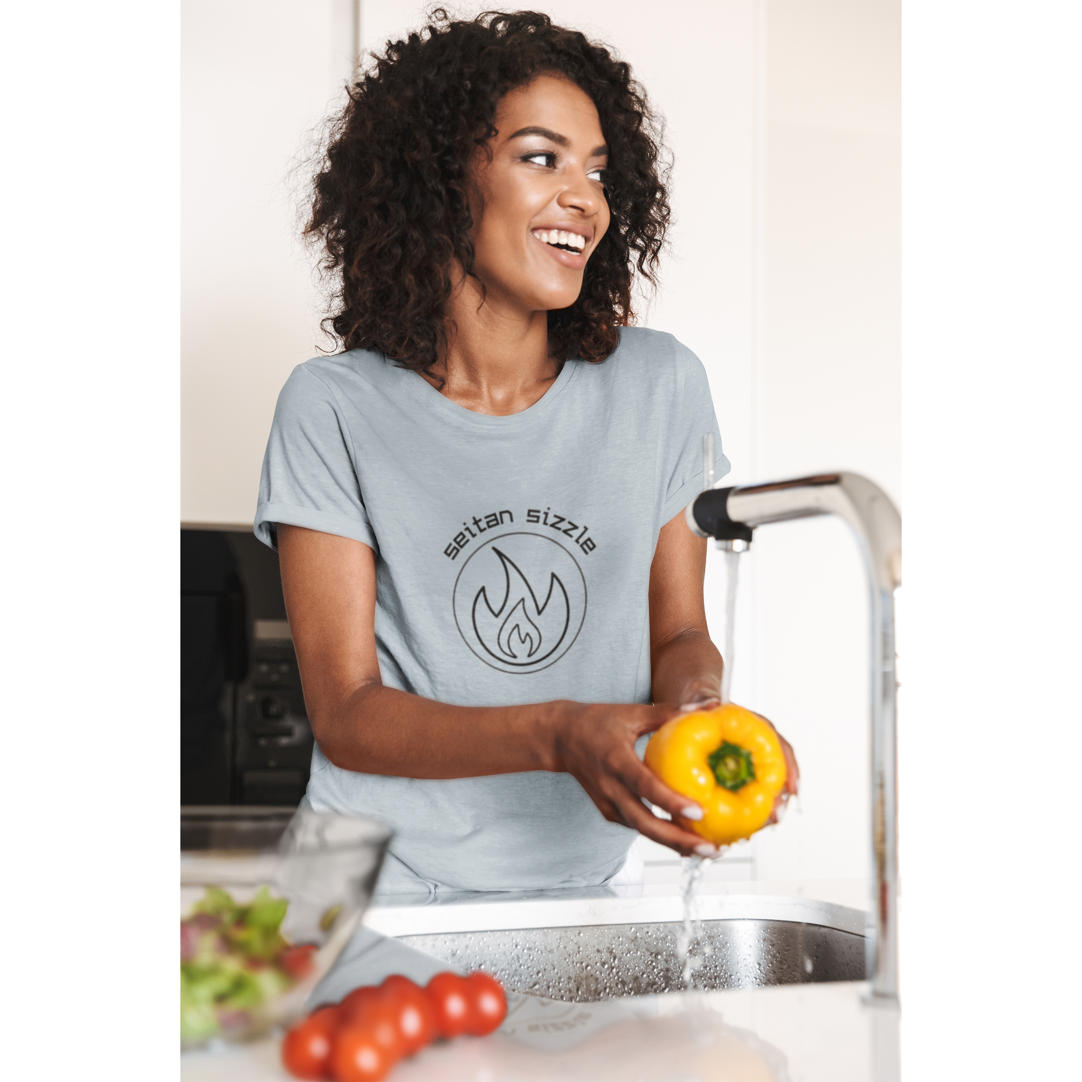 woman cooking seitan recipes wearing light blue colored vegan shirt with black graphic saying seitan sizzle over a circle with a flame design, from ethical clothing brands and companies that donate to nonprofits