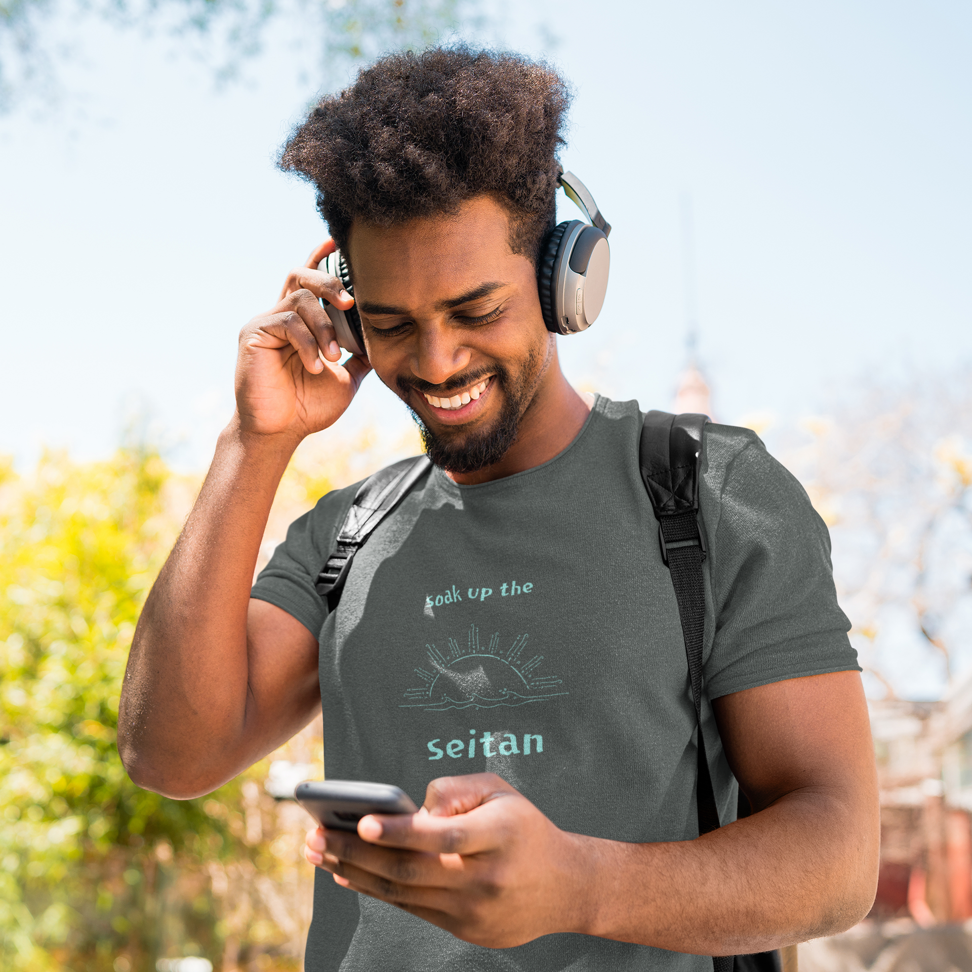 vegan t shirt in dark grey heather color with a teal design saying soak up the seitan worn by a man listening to music outside