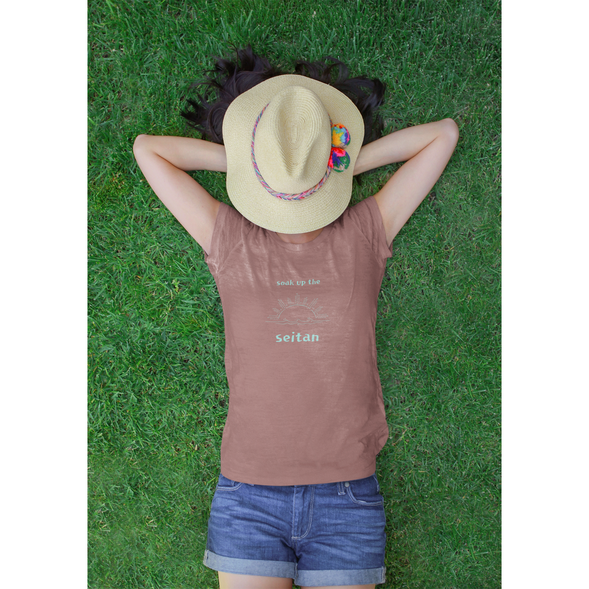 premium vegan t shirt in heather mauve with a teal design saying soak up the seitan worn by a woman laying in the grass