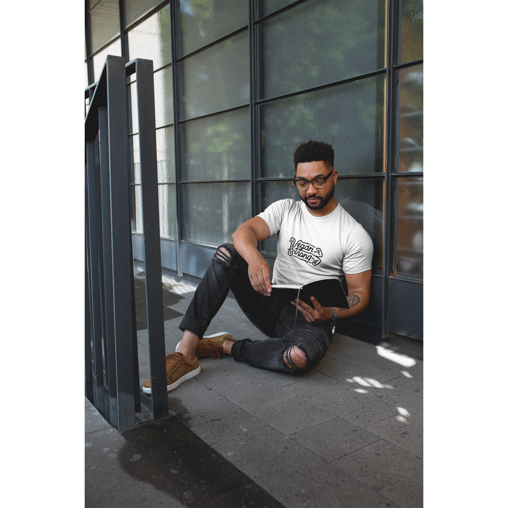 white vegan t shirt saying vegan strong worn by a muscular man sitting and reading