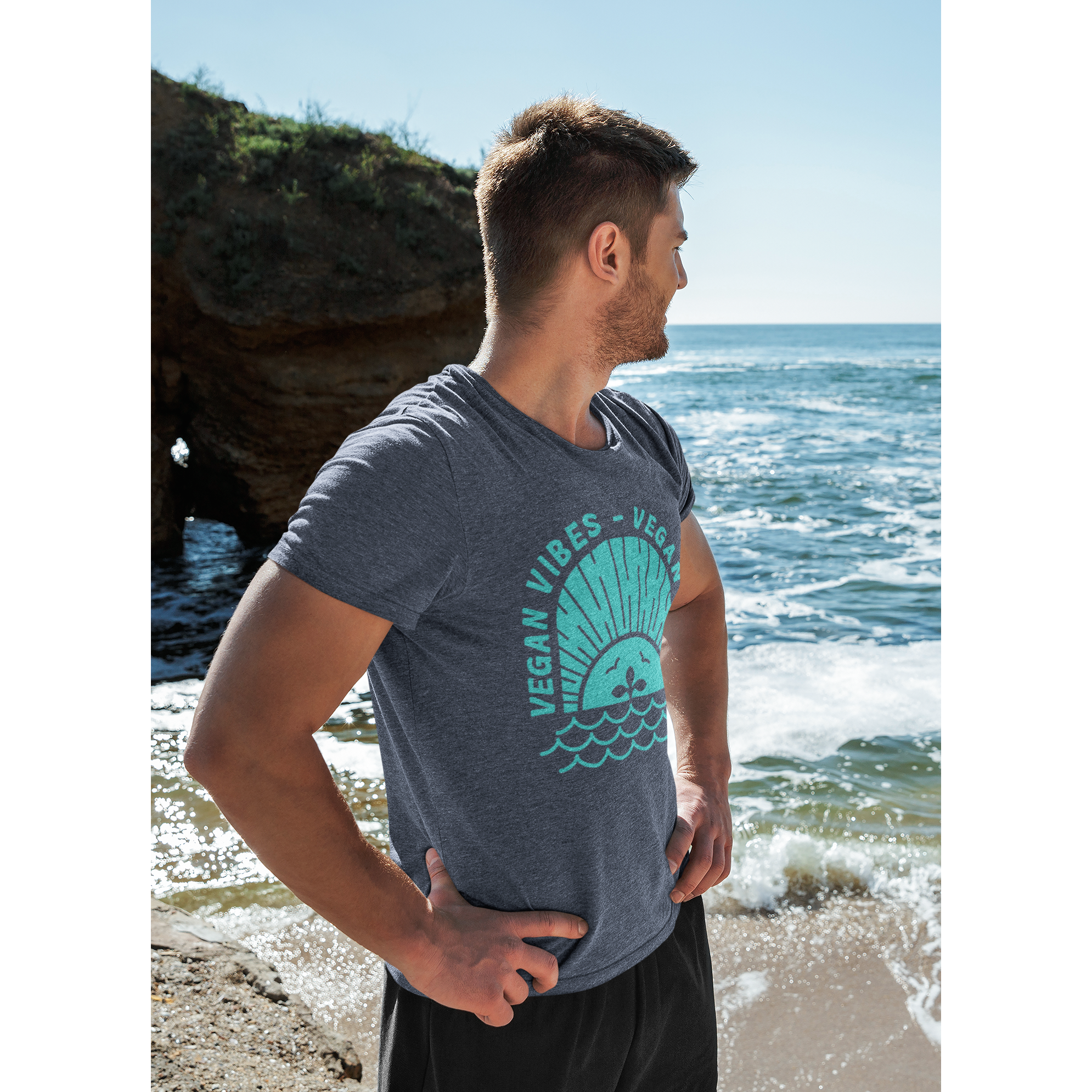 man on the beach wearing a vegan t shirt with a teal vegan vibes design on heather navy colored premium fabric