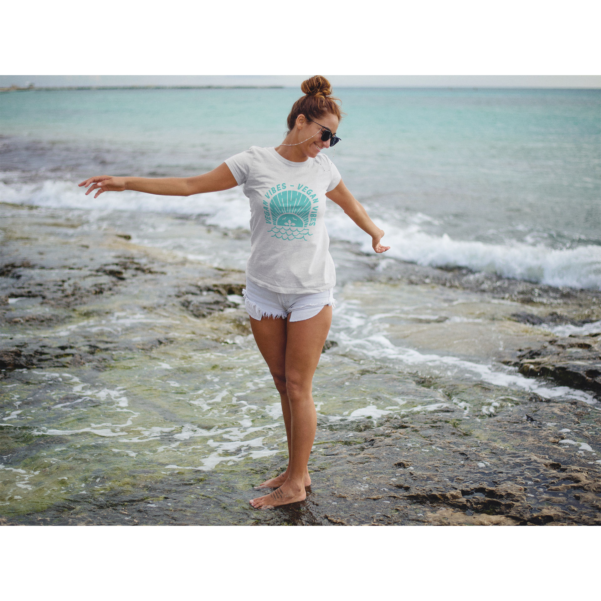 woman on a beach wearing a vegan vibes vegan tshirt with a teal design on a premium white cotton fabric