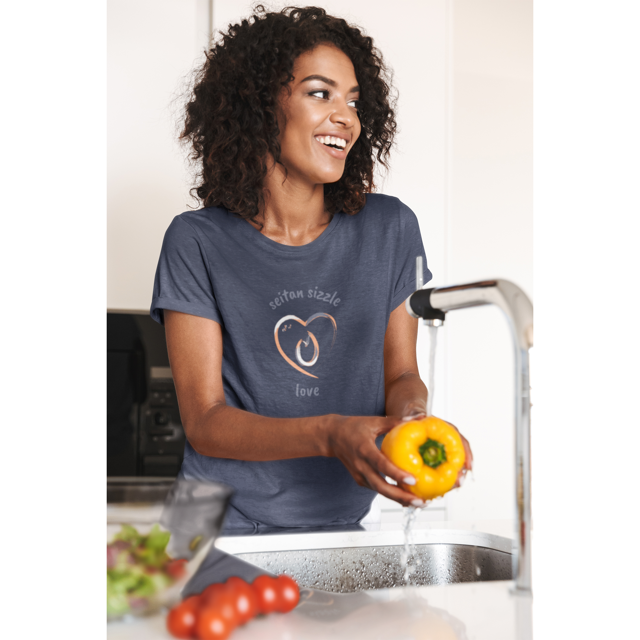 woman washing vegetables wearing a navy vegan t shirt with a brushed design saying seitan sizzle love and a heart